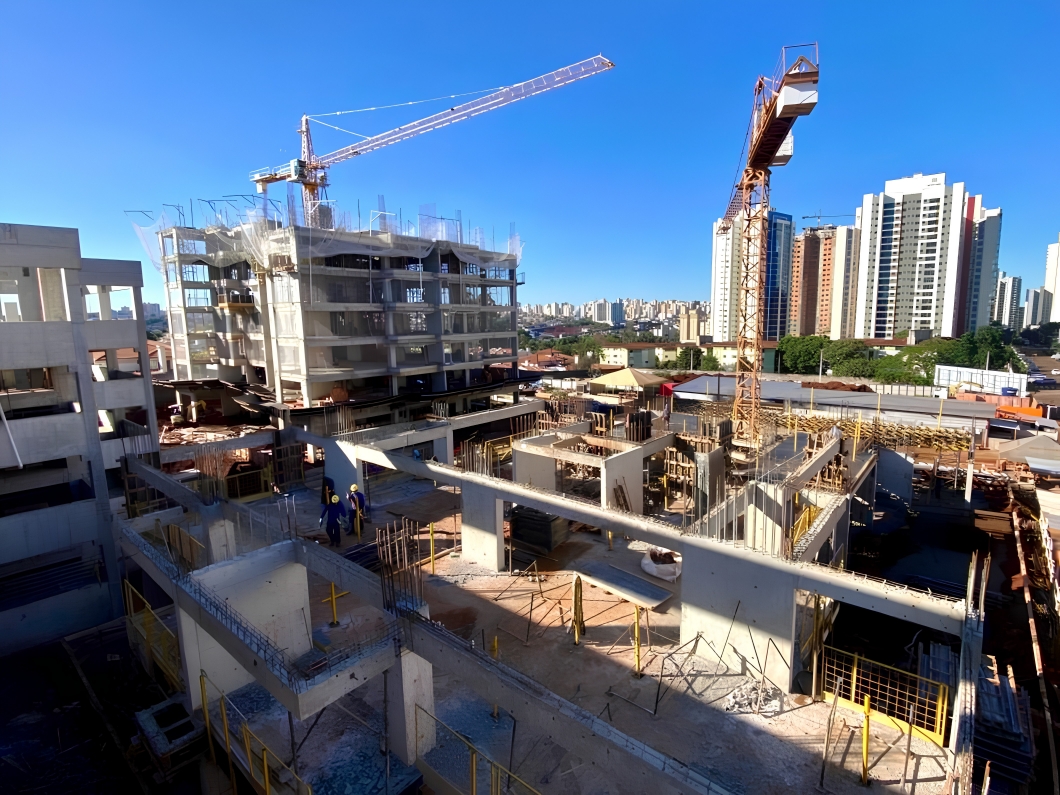 Vista aérea de obra com duas gruas e edifícios ao fundo